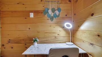 Interior de una cabaña de madera con una mesa de mármol, un adorno colgante de hojas, una pequeña planta en maceta y una lámpara de escritorio.