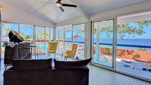 Habitación amplia con un gran ventanal corredero que da a una zona de piscina, ventilador de techo y vistas al océano.