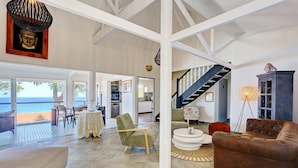 Amplia sala de estar con vista al mar, una escalera y un comedor con mesa y sillas.