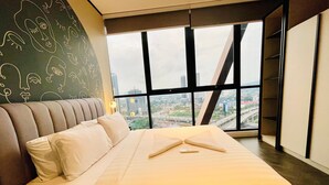 A modern hotel room with a large bed, a view of the cityscape through floor-to-ceiling windows, and a unique wall design.