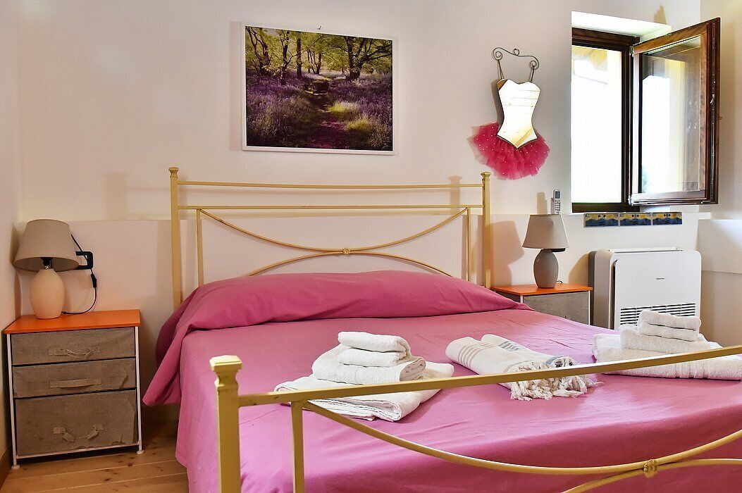 A bedroom with a bed, a nightstand, a lamp, a mirror, and a wall-mounted picture.