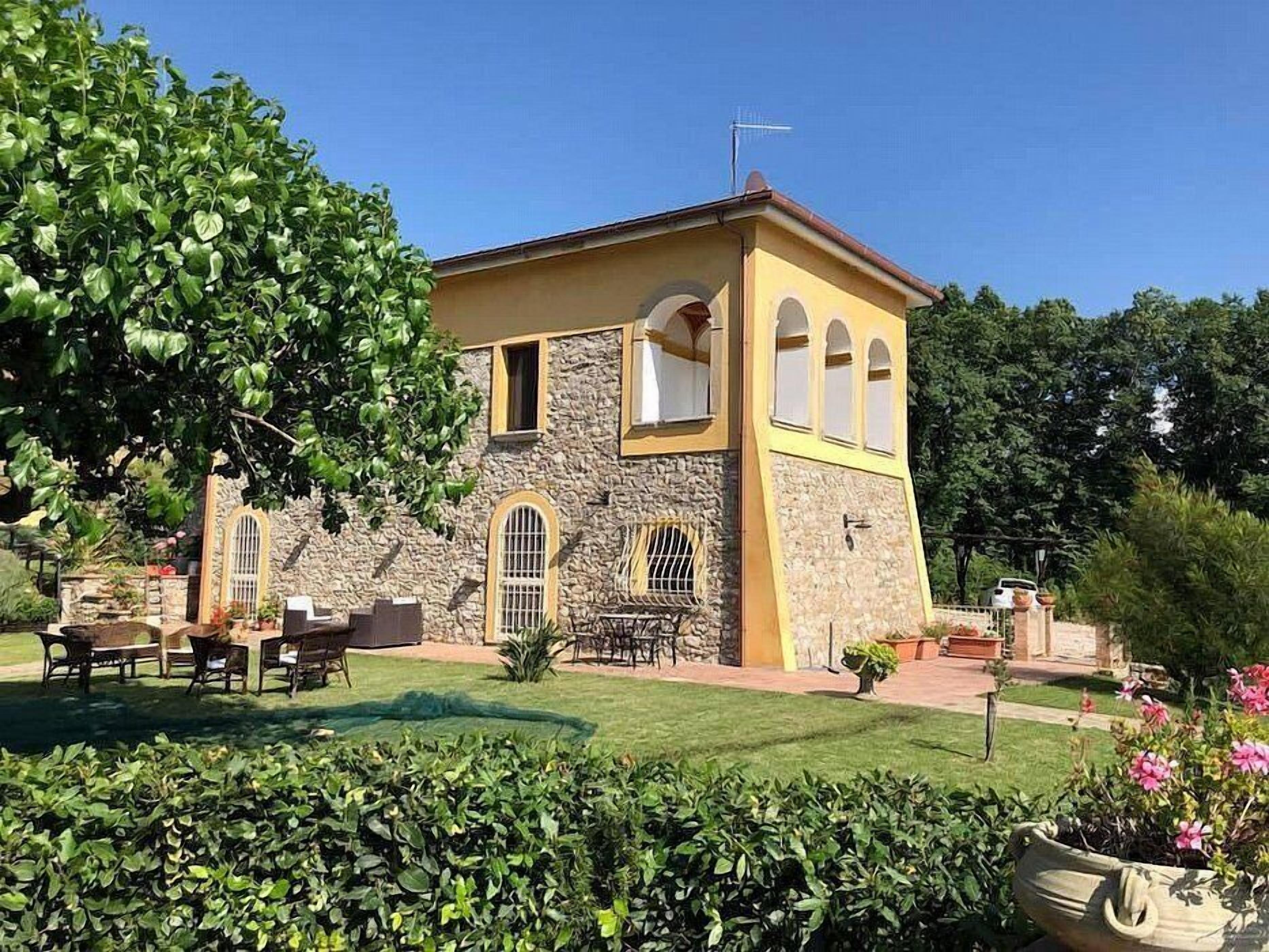 A two-story building with stone and yellow walls, a stone staircase, and a patio with outdoor furniture.
