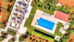 Vista aérea de una propiedad con piscina, varias zonas de estar al aire libre y un edificio con techo rojo.