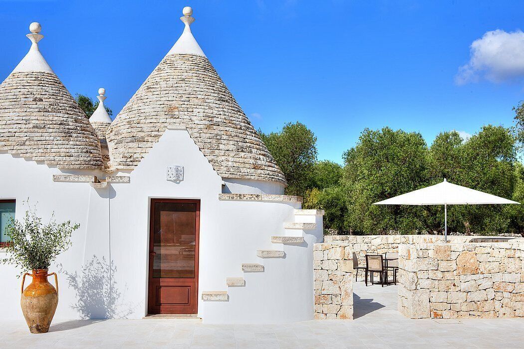 A building with conical roofs, a wooden door, and a stone wall with steps leading to a patio area.