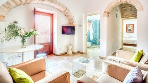 Una sala de estar moderna con televisor, asientos cómodos, una mesita y vistas a un área exterior a través de un arco.