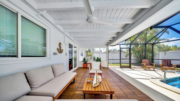 A covered outdoor area with a wooden deck, a pool, and a seating area with a sofa and chairs.