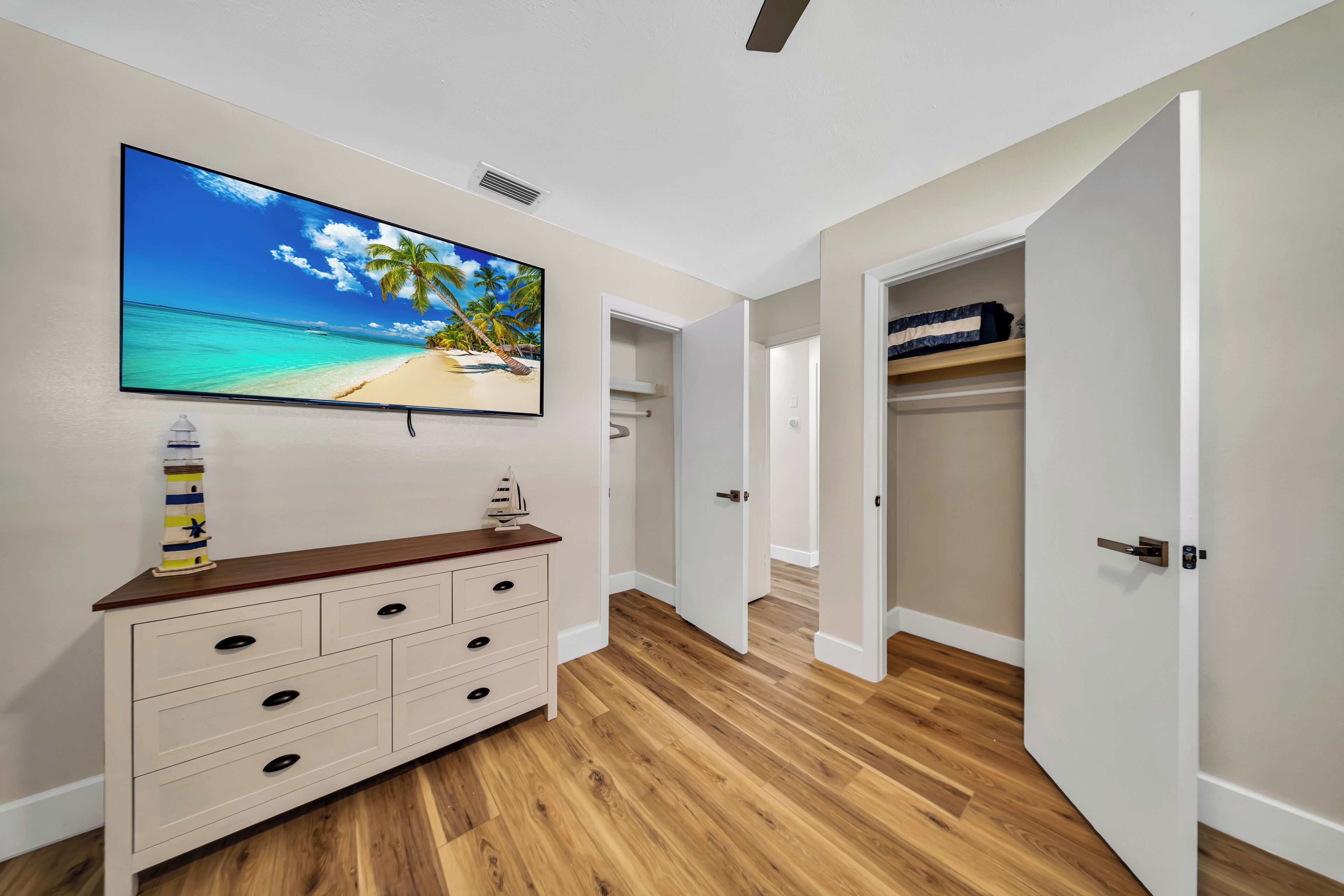 Ein Zimmer mit Holzboden, einem weißen Schminktisch, einem an der Wand befestigten Fernseher und einem Kleiderschrank mit Ablagefläche.