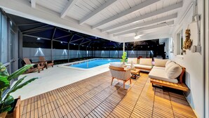 A spacious indoor pool area with a wooden deck, a lounge area with a sofa and chairs, and a ceiling with exposed beams.