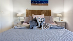 A neatly made bed with a quilted cover, two bedside tables with lamps, a woven headboard, and a painting of the ocean on the wall. - Winahost Apartment Jávea (Jávea)