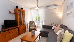 A living room with a television, wooden cabinet, sofa, and a dining area with a chair and table. - Winahost Apartment Jávea (Jávea)