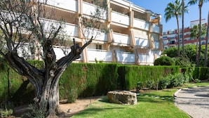 A well-maintained garden with a large tree, neatly trimmed hedges, and a stone feature. - Winahost Apartment Jávea (Jávea)