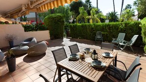 An outdoor patio with a wooden table set for dining, surrounded by wicker chairs and a striped awning. - Winahost Apartment Jávea (Jávea)