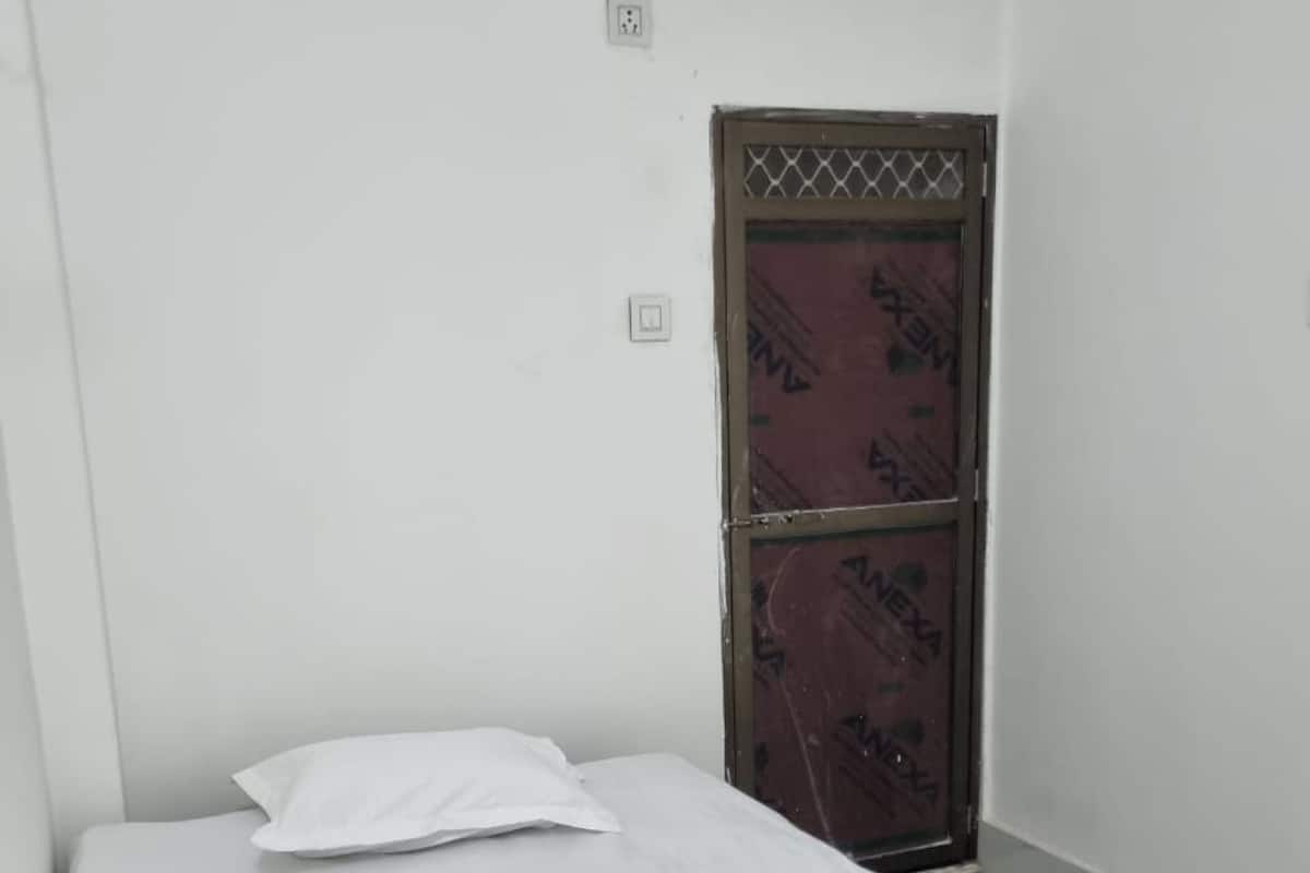 Una cama individual con colchón y almohada blancos en una habitación con paredes blancas y una puerta de madera.