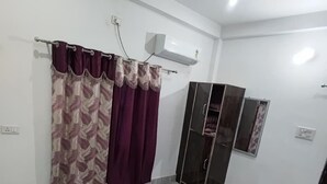 A room with a ceiling fan, an air conditioning unit, a wardrobe, and a floral-patterned rug. - Shree Shyam Paying Guest House (Varanasi)