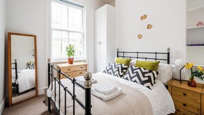 Ein Schlafzimmer mit einem Bett, einem Nachttisch aus Holz, einem Spiegel und einem Fenster mit Blick auf die Straße.