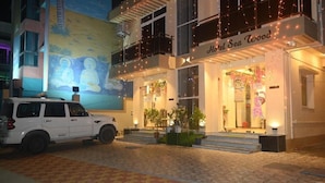 A hotel named "Hotel Sea Wood" with a mural of meditating figures on the wall, a white SUV parked in front, and a check-in counter visible. - Hotel Sea Wood (Digha)