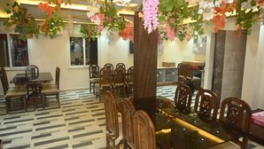A dining area with a glass table surrounded by wooden chairs, a patterned floor, and hanging floral decorations. - Hotel Sea Wood (Digha)