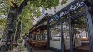 A hotel with outdoor seating and a large tree in front. - Hotel Riverside (Skopje)