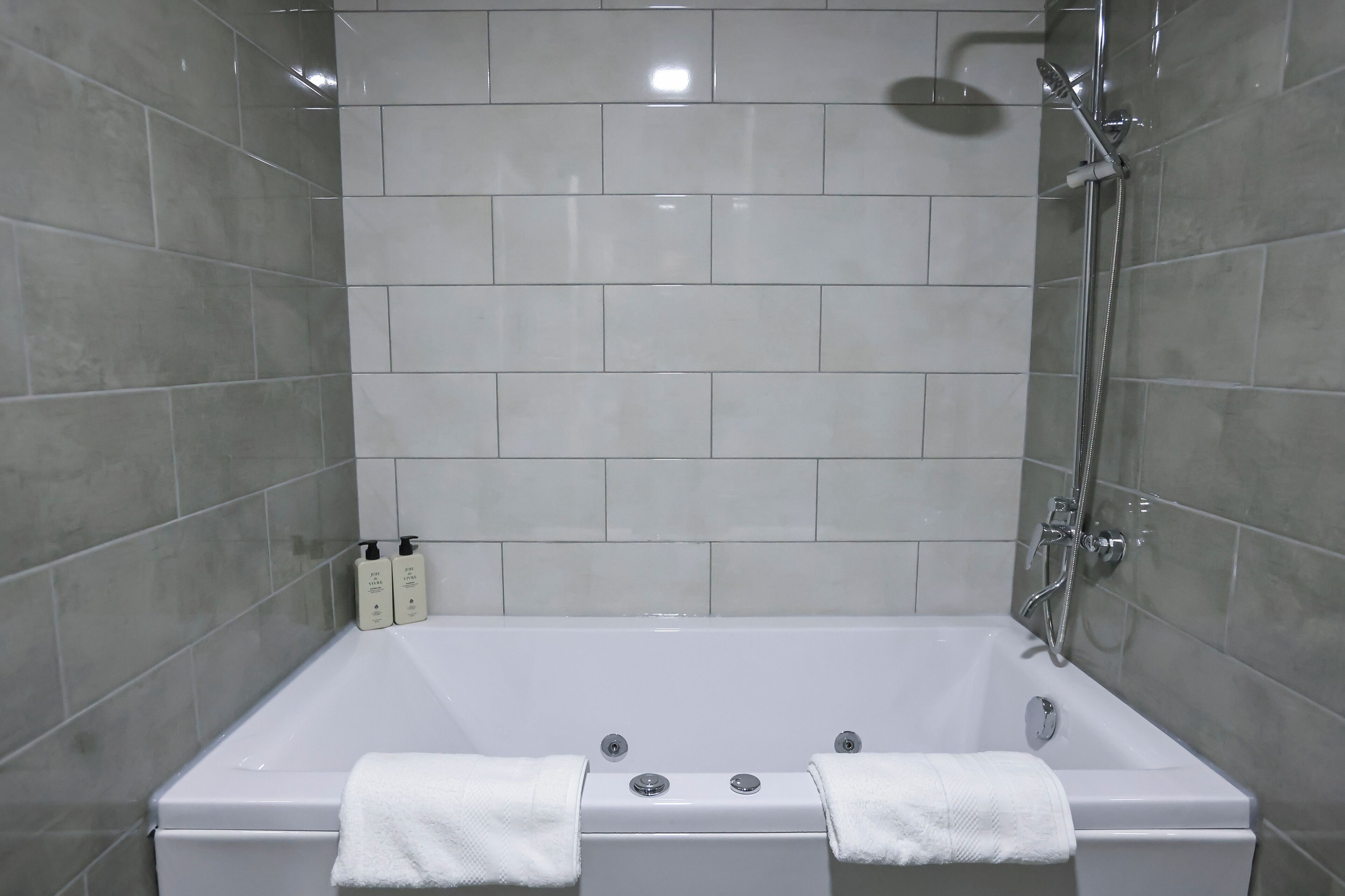 A modern bathroom with a white bathtub, a showerhead, and two bottles of shampoo on the wall.