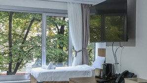 A modern hotel room with a bed, a desk, a chair, a TV, and a window with curtains. - Hotel Riverside (Skopje)