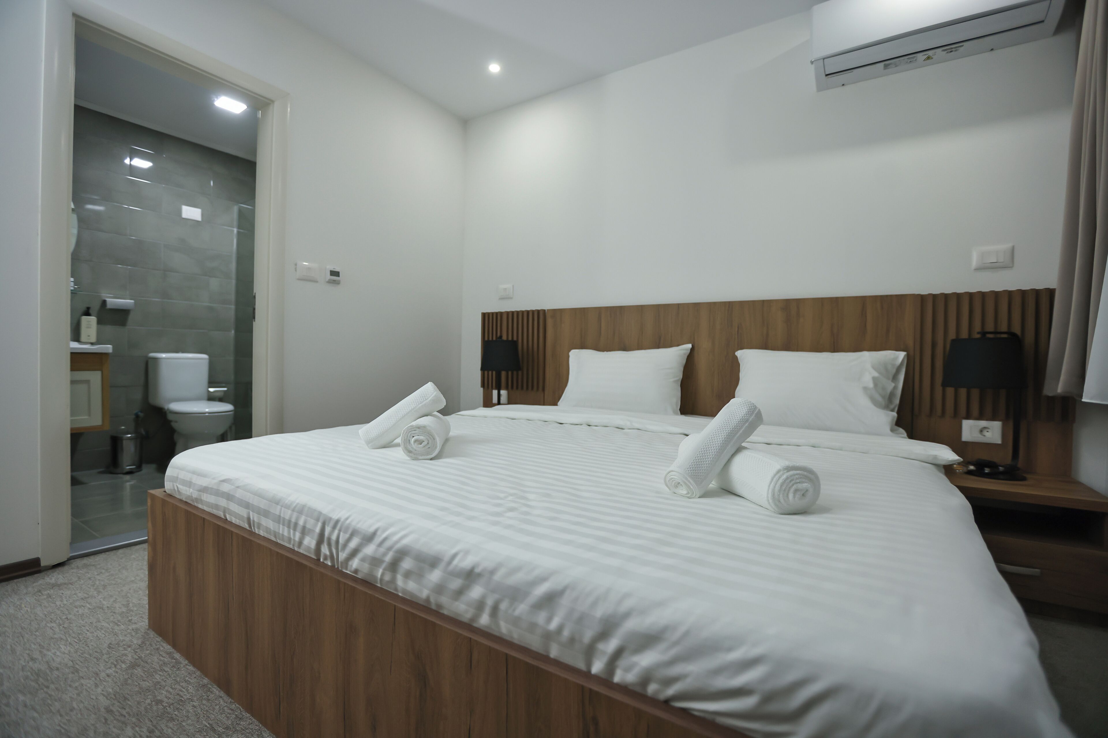 Una habitación de hotel moderna con una cama grande, cabecero de madera y dos mesitas de noche con lámparas.