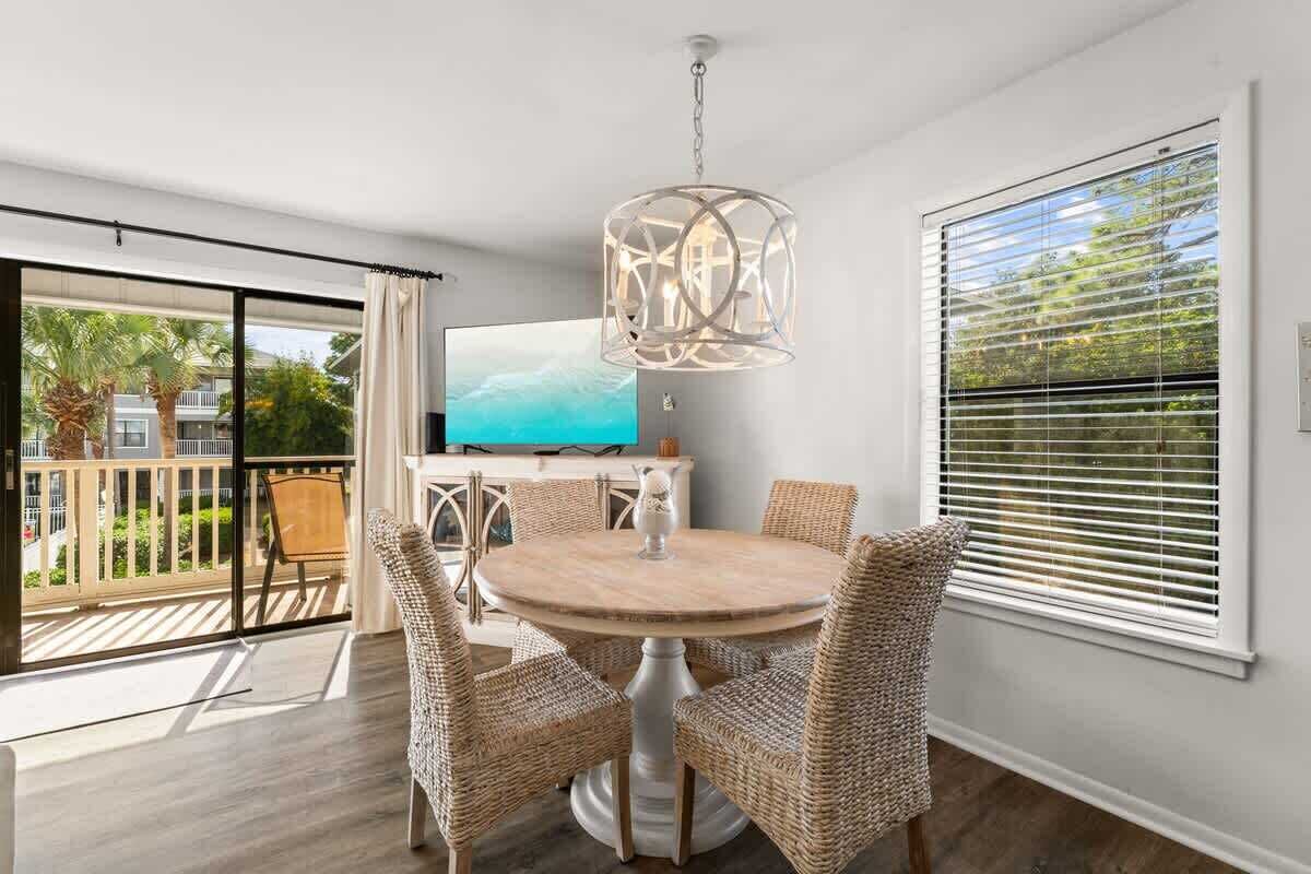A room with a round table, wicker chairs, a television, and a large window with blinds.
