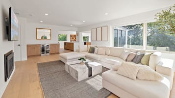 A modern living room with a large sectional sofa, a marble coffee table, and a view of the outdoors through large windows.