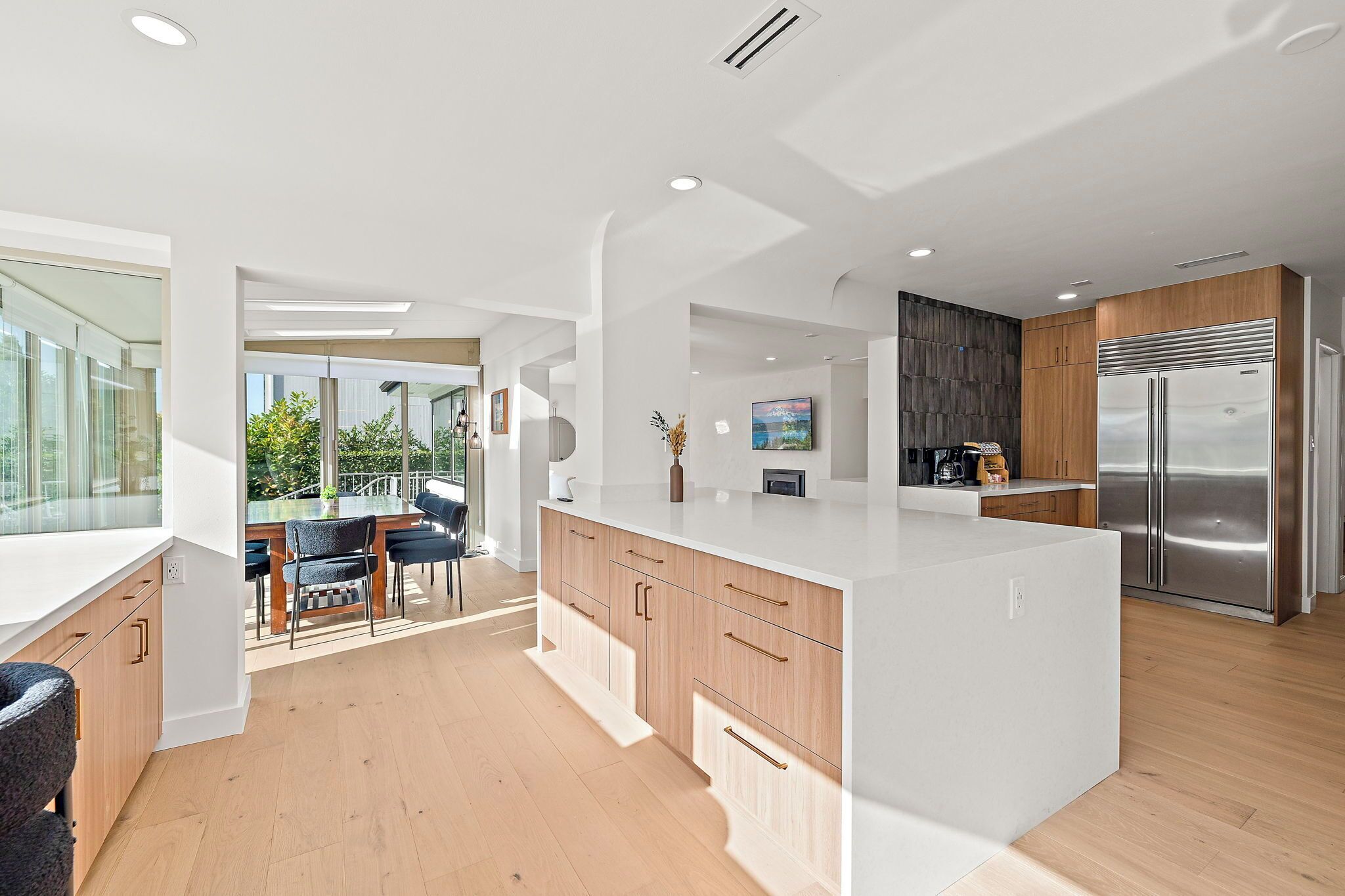 A modern kitchen with a large island, wooden cabinets, and a stainless steel refrigerator.