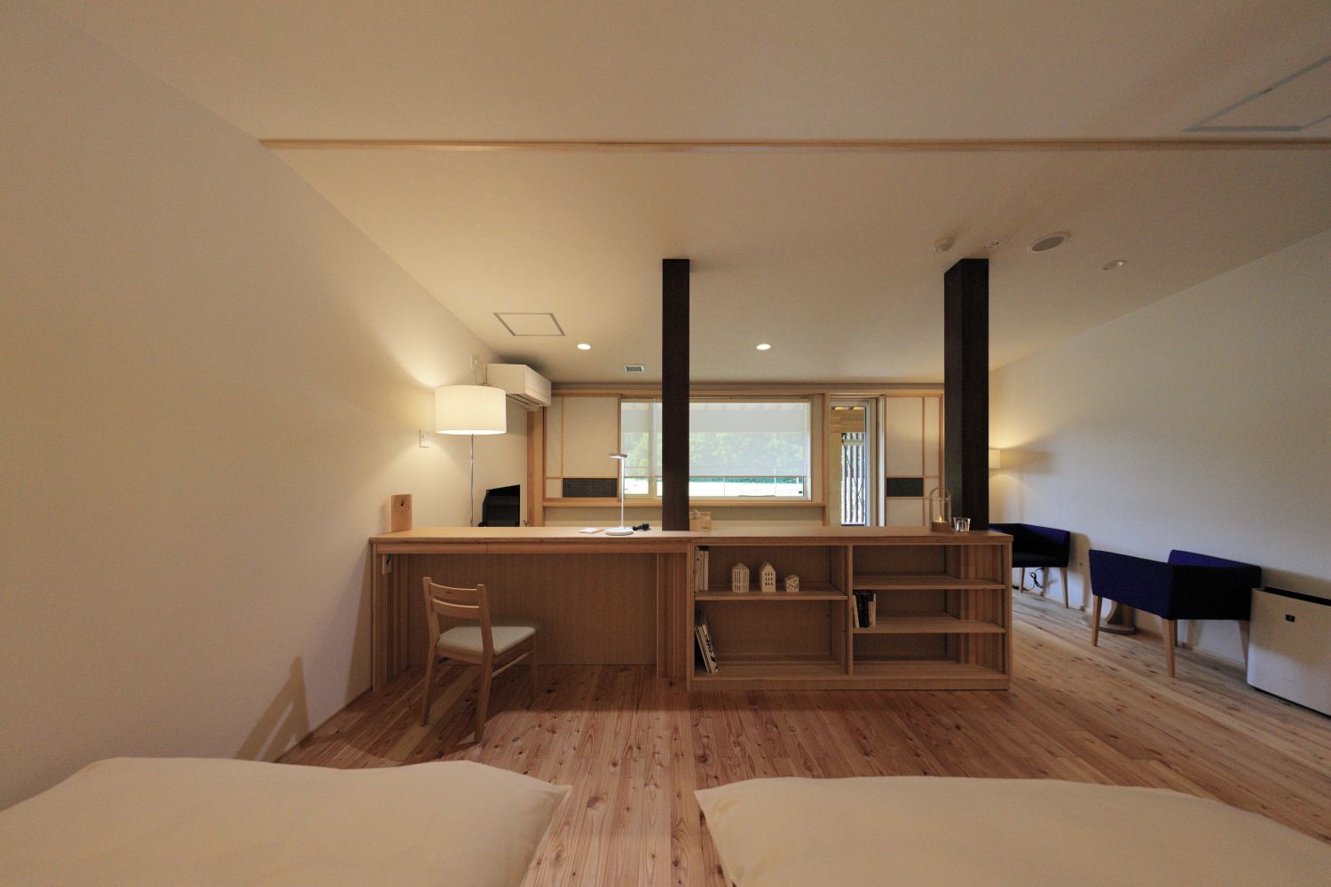 A modern room with a wooden desk, a chair, a bed, and a small table with a lamp.