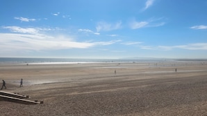 A wide beach with people walking, a clear sky, and distant mountains.
