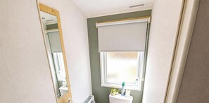 A bathroom with a toilet, sink, mirror, and window with a blind. - MKRJ LUXURY - Parkdean Camber Sands - Sleeps 8 - Pet Friendly - lbl (Camber)