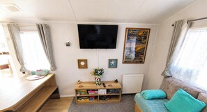 A compact living space with a flat-screen TV, a sofa, a wooden table, and a small bookshelf. - MKRJ LUXURY - Parkdean Camber Sands - Sleeps 8 - Pet Friendly - lbl (Camber)