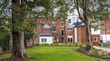 A residential building with a brick facade, a small garden, and a tree in the foreground.
