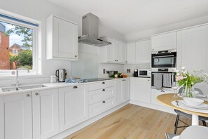 Una cocina moderna con armarios blancos, horno empotrado y comedor con mesa de madera.
