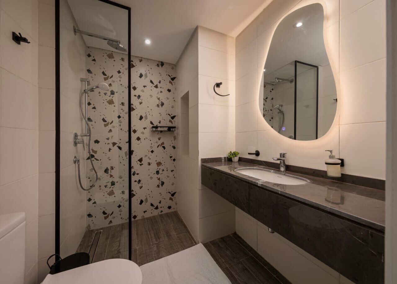 A modern bathroom with a glass-enclosed shower, a large mirror, and a marble countertop.
