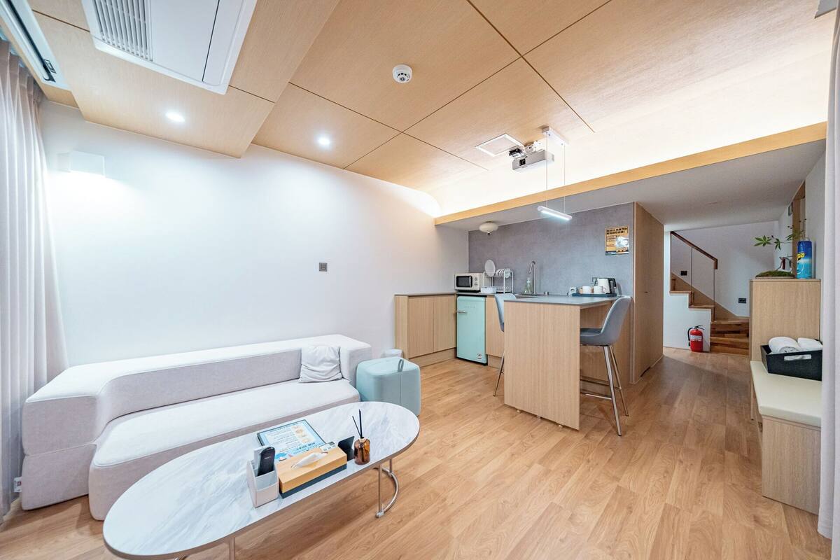 Un espacio habitable moderno y funcional con sofá, pequeña cocina y mesa de comedor.