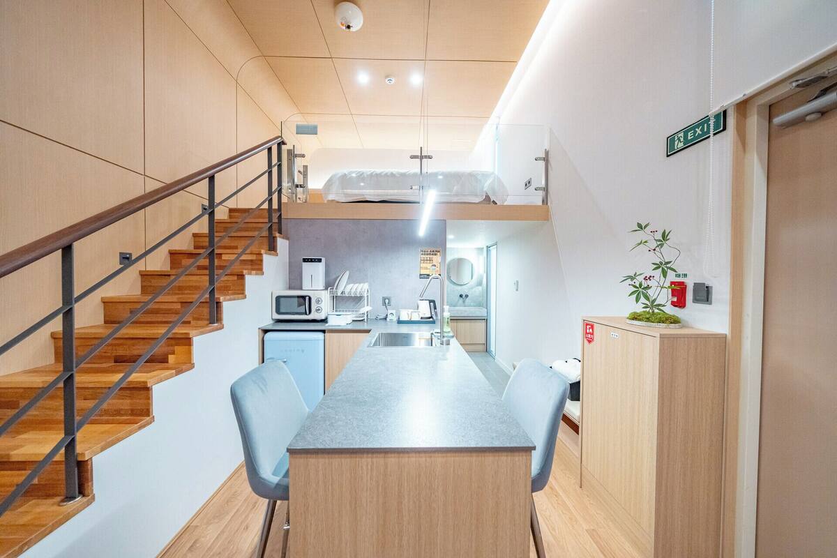 Una habitación de hotel compacta con kitchenette, zona de comedor y una escalera.