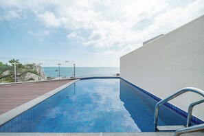 Une piscine avec vue sur la mer, une terrasse en bois et un mur blanc.
