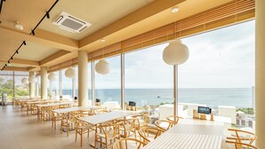 A spacious dining area with tables and chairs, large windows offering a view of the sea, and a ceiling with recessed lighting. - Ocean Bliss (Ulsan)