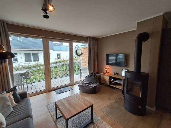 A modern living room with a sofa, a coffee table, a TV, a fireplace, and a balcony with a view of buildings.