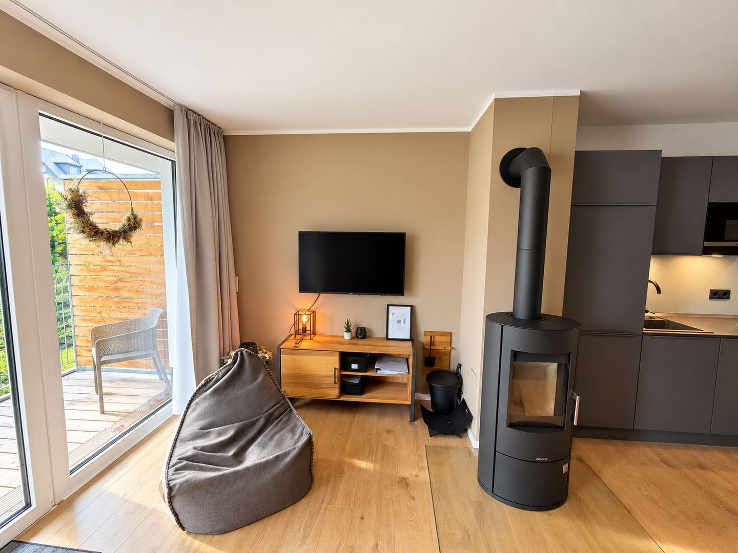 Een moderne woonkamer met een flatscreen televisie, een houtkachel, een relax fauteuil en een schuifpui naar een balkon.