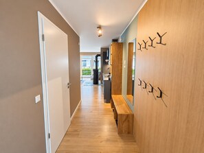 A hallway with wooden flooring, a bench, and wall-mounted hooks.