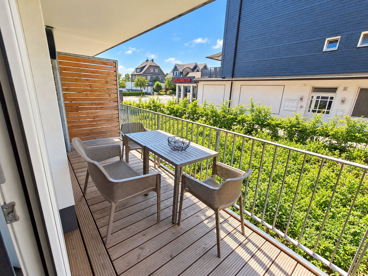 A balcony with a table and chairs, a wooden fence, and a view of houses and greenery.