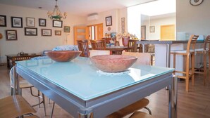 A dining area with a glass-top table, wooden chairs, and a chandelier. - Golf-view villa with pool (Chiclana de la Frontera)