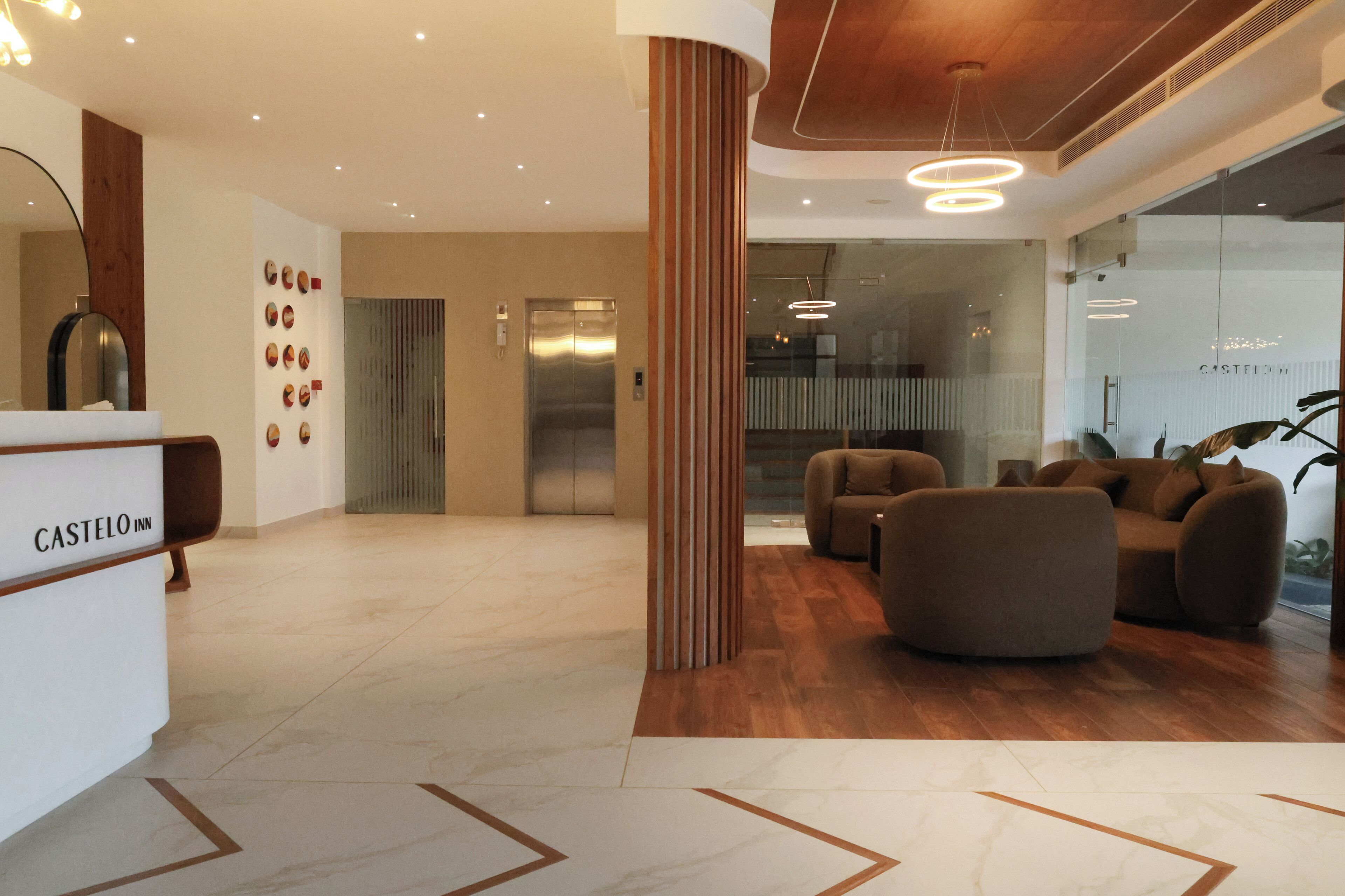Un hall d’hôtel comprenant un comptoir d’accueil, une colonne en bois, un espace salon avec des canapés et un ascenseur.