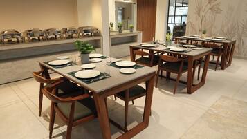 Comedor con varias mesas dispuestas para comensales, con sillas de madera y una planta en maceta en el centro.