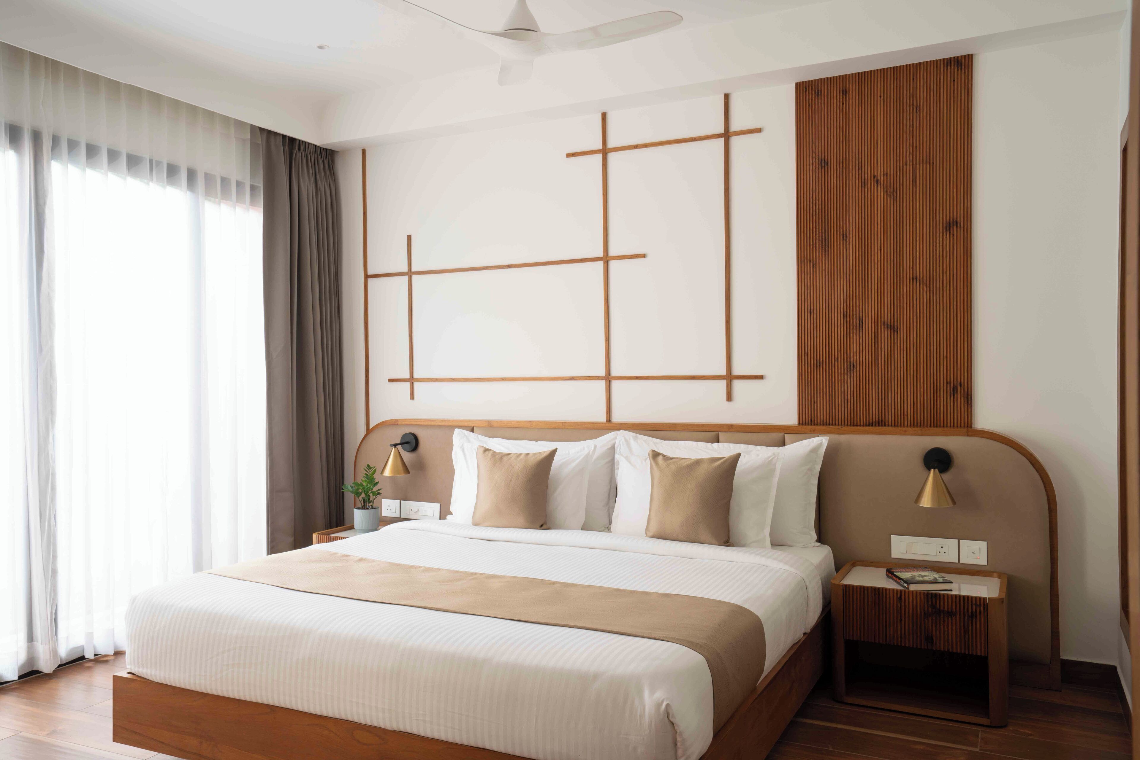 A modern hotel room with a large bed, wooden headboard, and a geometric wall design.