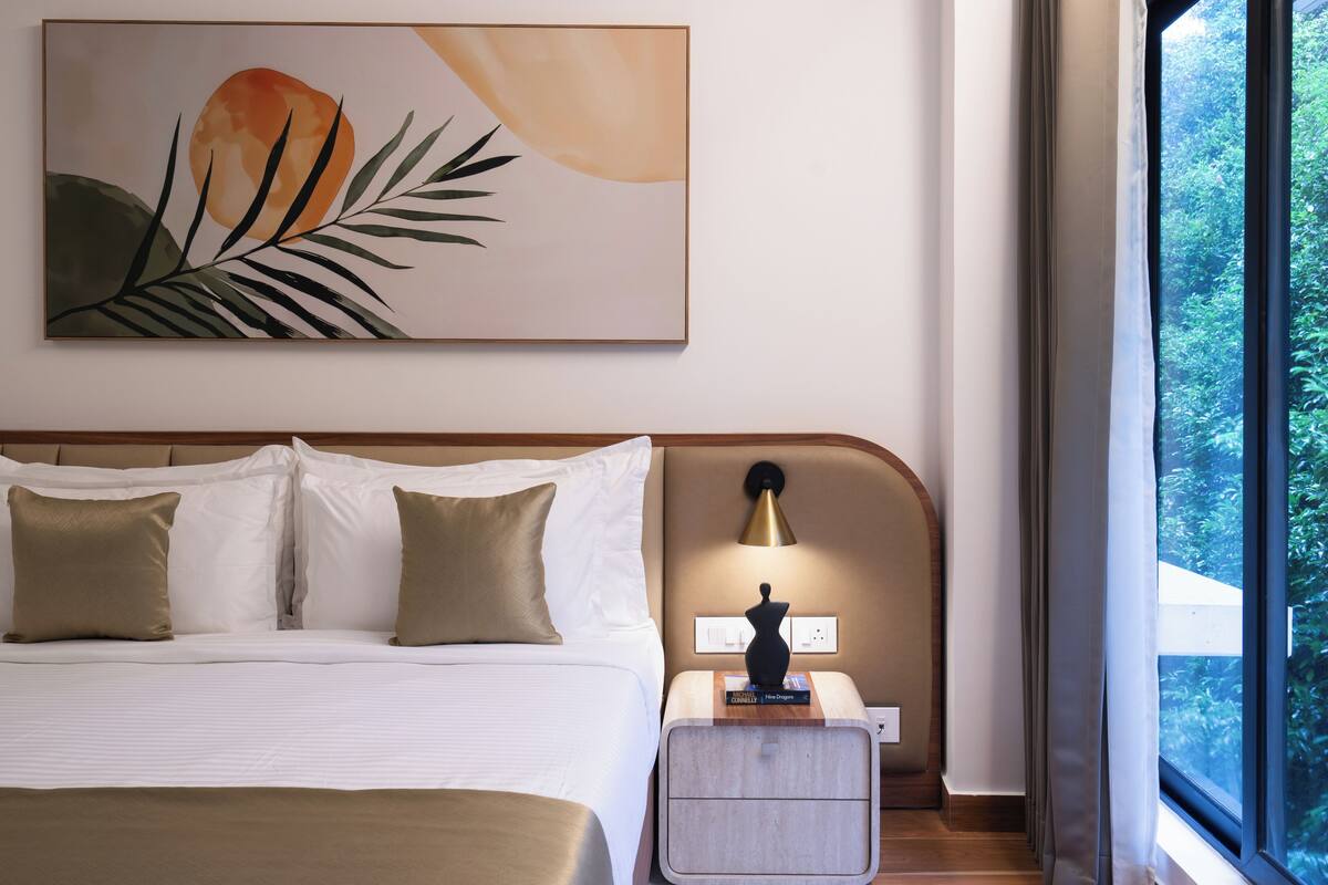 A hotel room with a bed, nightstand, lamp, and a painting on the wall.