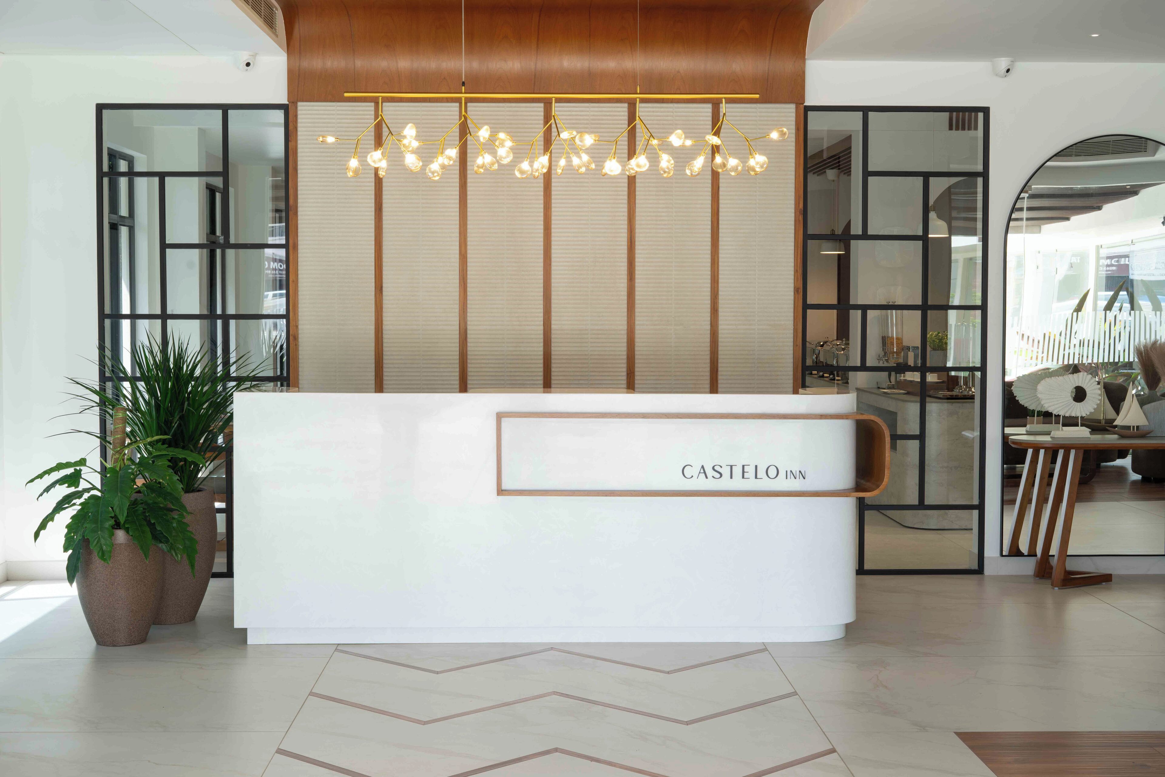 A reception desk with a sign reading "CASTELO INN" in a modern lobby with potted plants and a decorative light fixture.