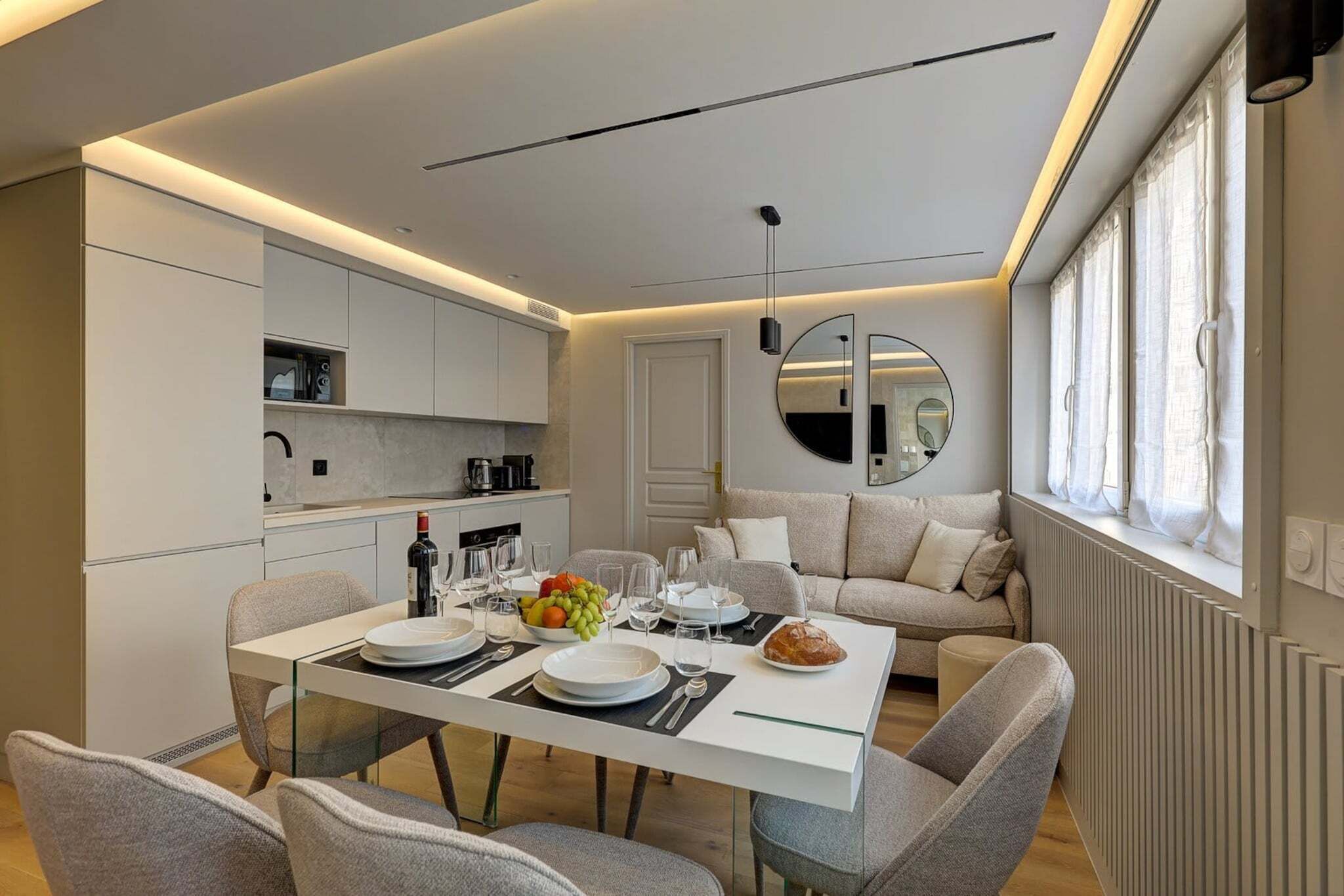 Une cuisine moderne avec des meubles blancs, une table à manger pour quatre personnes et un canapé dans l’espace salon.